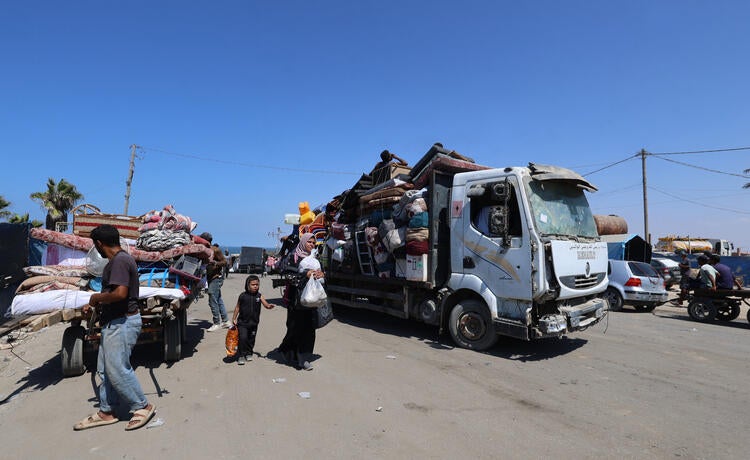 A cart and a truck are loaded up with belongings as people stand on the street holding bags